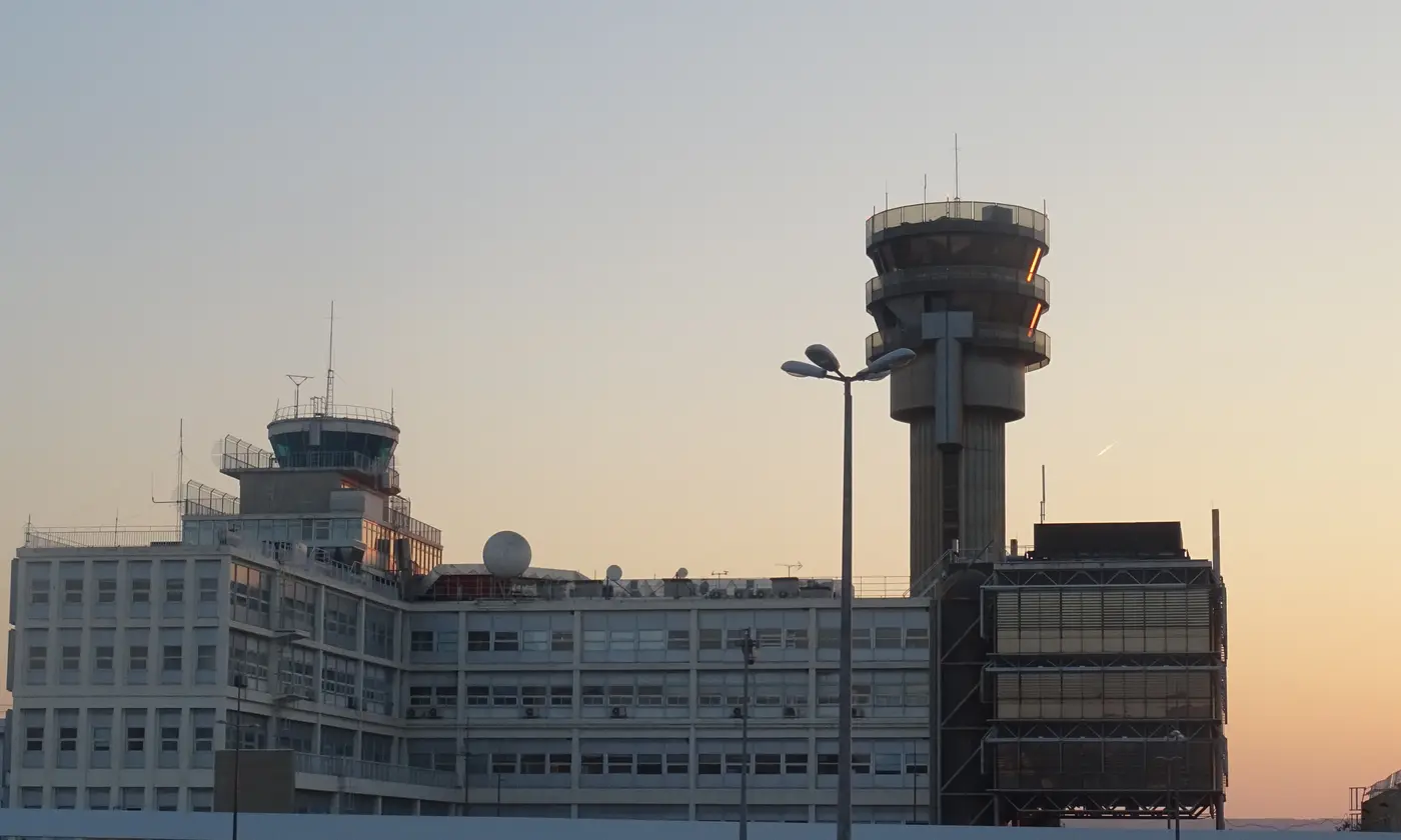La tour de contrôle de l'aéroport Marseille-Provence et le bâtiment administratif se découpent sur un ciel orangé de fin de journée.