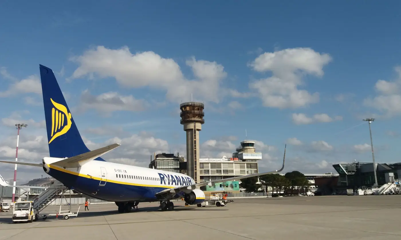 Un Boeing 737-800 de Ryanair stationné sur le tarmac de l'aéroport Marseille-Provence en plein soleil, la tour de contrôle et l'aérogare derrière lui.