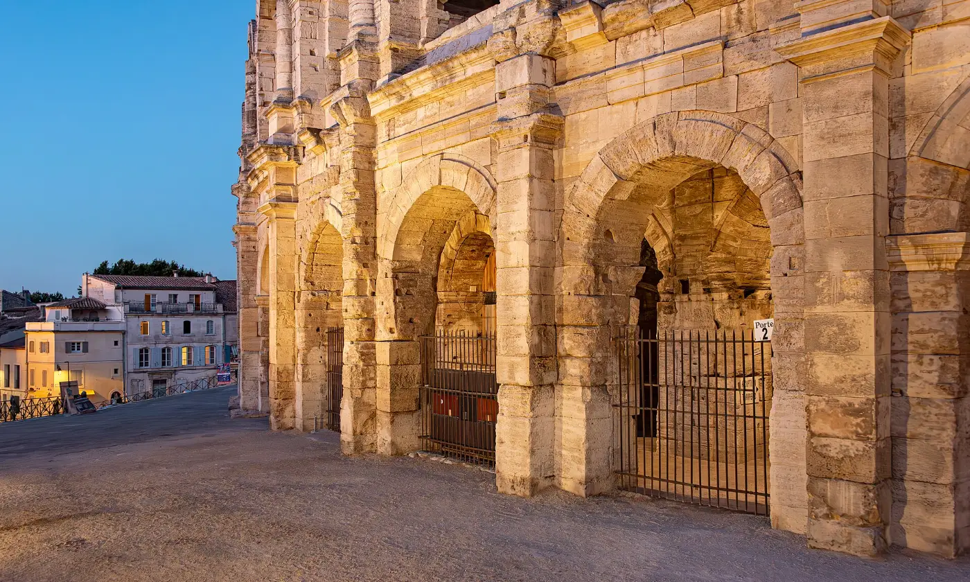 Arcades des arènes d'Arles éclairées à l'heure bleue, façades du vieil Arles au fond
