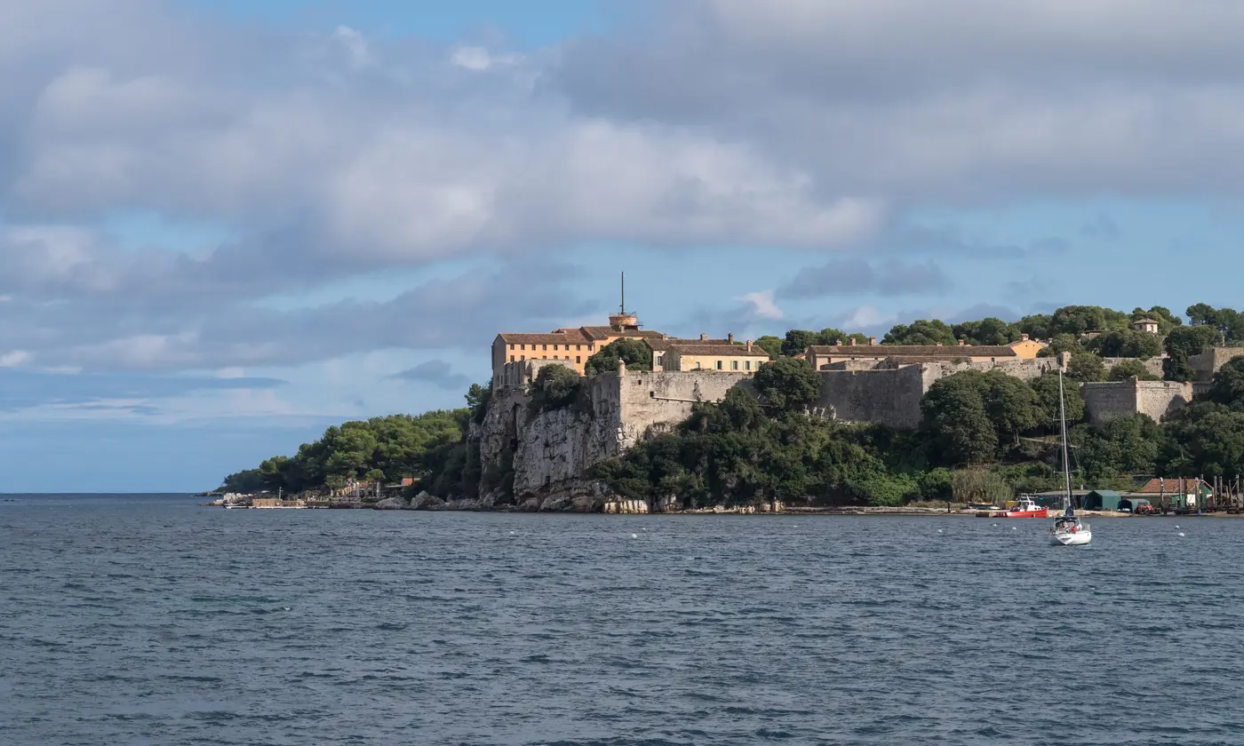 Le Fort Royal de l'île Sainte-Marguerite dressé sur sa falaise face à la mer, un voilier au mouillage, îles de Lérins, Cannes