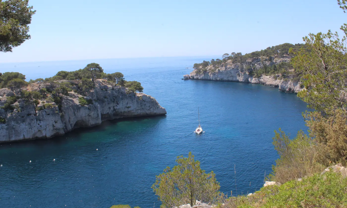 Voilier glissant entre les falaises calcaires et l'eau bleu profond à l'entrée de la calanque de Port-Miou, Cassis