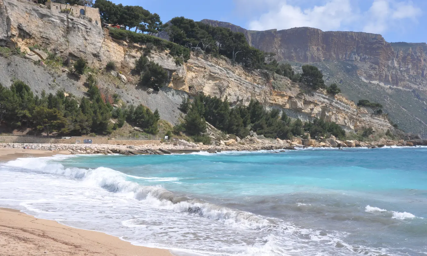 Vague turquoise sur la plage de la Grande Mer, sous les remparts du château et les falaises du cap Canaille, Cassis