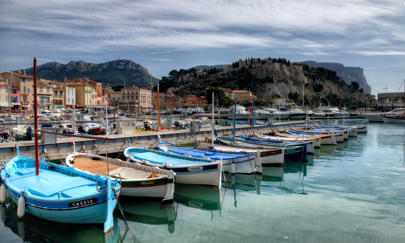 Barquettes de pêche colorées au premier plan et vue d'ensemble du village dominé par son château et le cap Canaille, Cassis