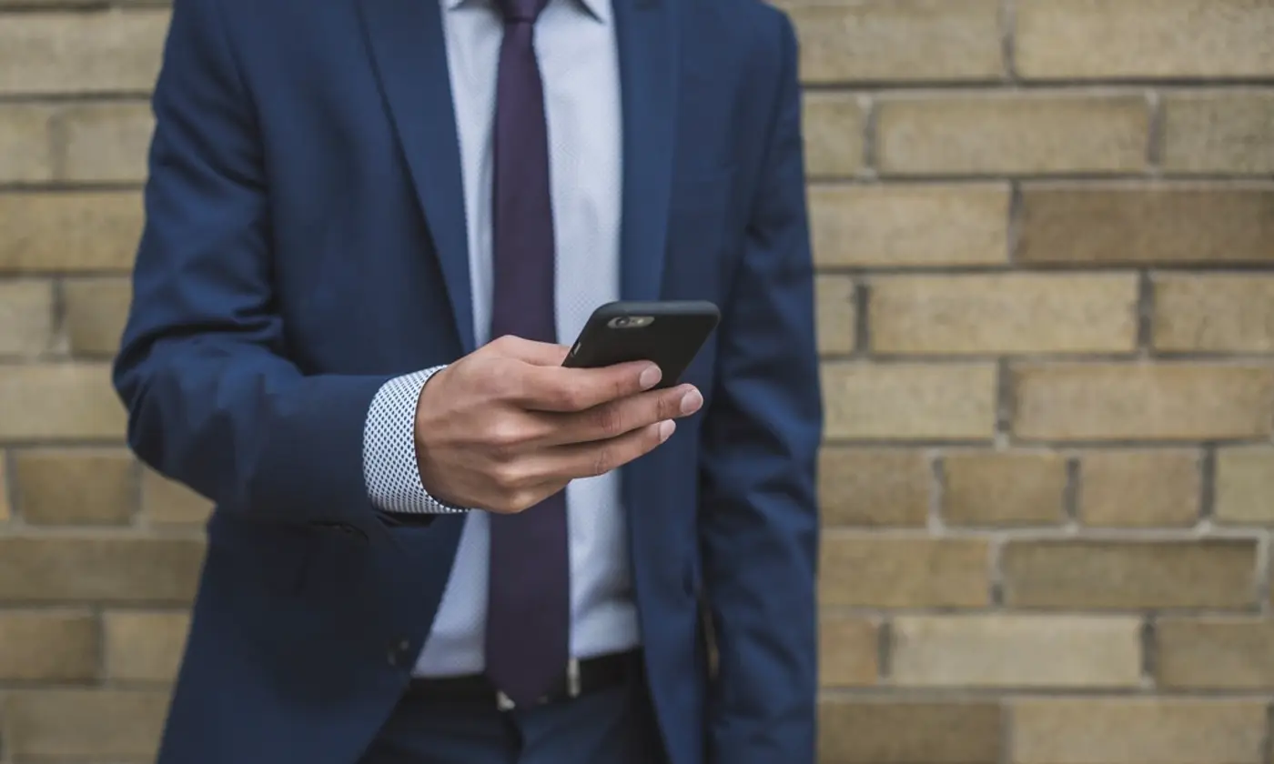 Homme d'affaires en costume bleu marine et cravate consultant son smartphone devant un mur de briques