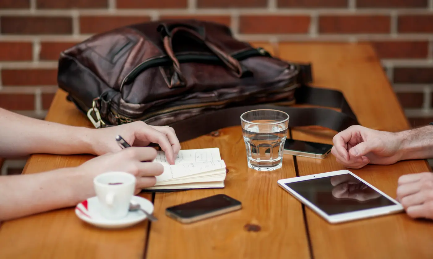 Réunion de travail autour d'une table en bois : prise de notes, tablette, téléphones et café