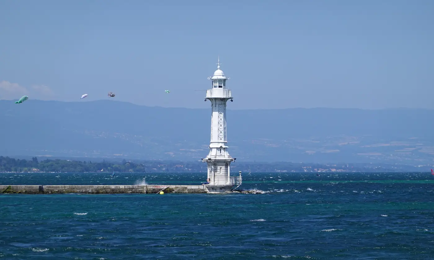 Le phare blanc des Pâquis au bout de sa jetée, sur les eaux bleu profond du lac Léman, Genève