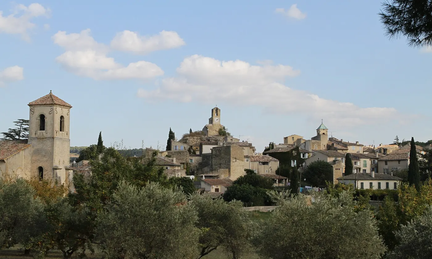 Le village de Lourmarin, son beffroi et ses clochers derrière une rangée d'oliviers