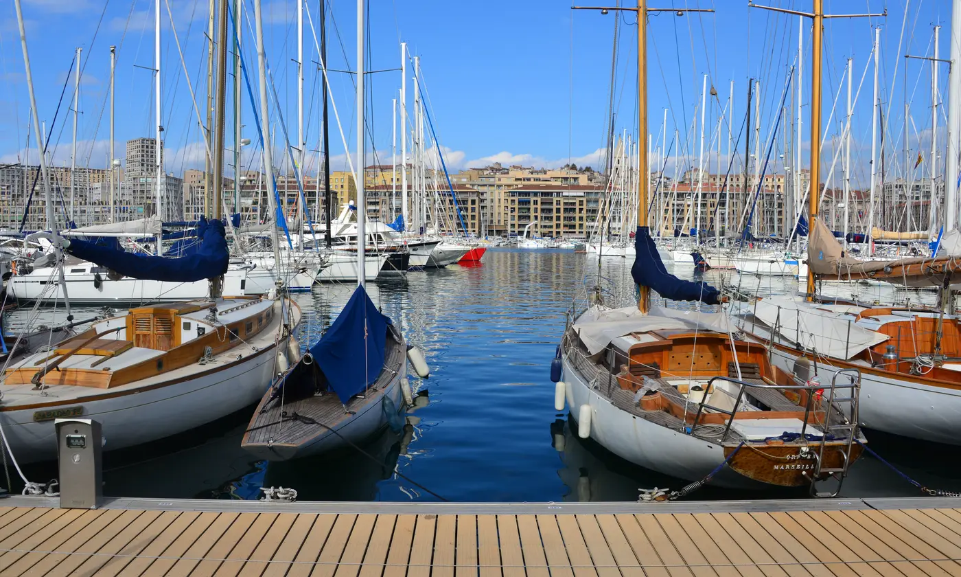 Voiliers en bois amarrés au ponton du Vieux-Port de Marseille, avec les façades des quais sous un ciel bleu.