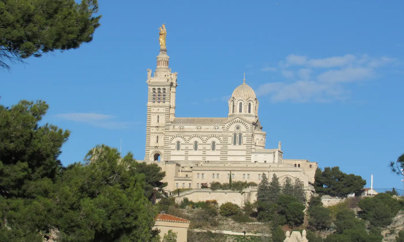 La basilique Notre-Dame de la Garde et sa Vierge dorée au sommet de la colline, entourée de pins.