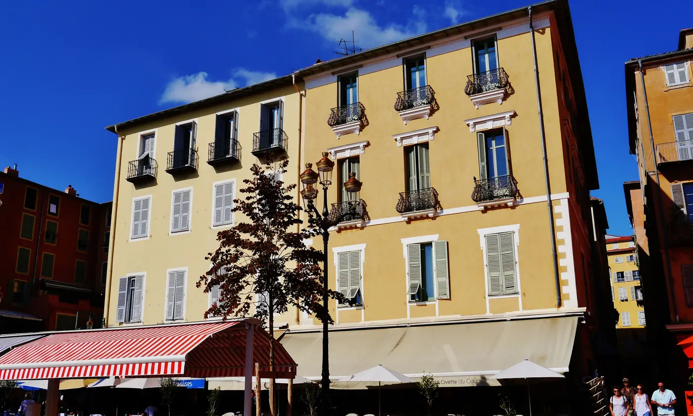 Façades ocre, balcons en fer forgé et stores rayés des terrasses du cours Saleya, au cœur du Vieux-Nice