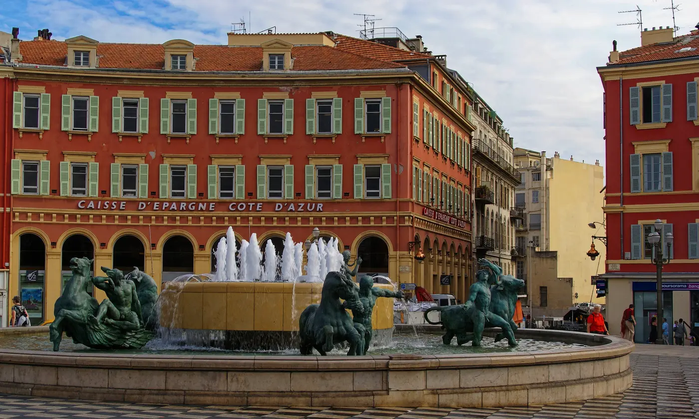 La fontaine du Soleil et ses statues de bronze devant les façades rouges de la place Masséna, Nice