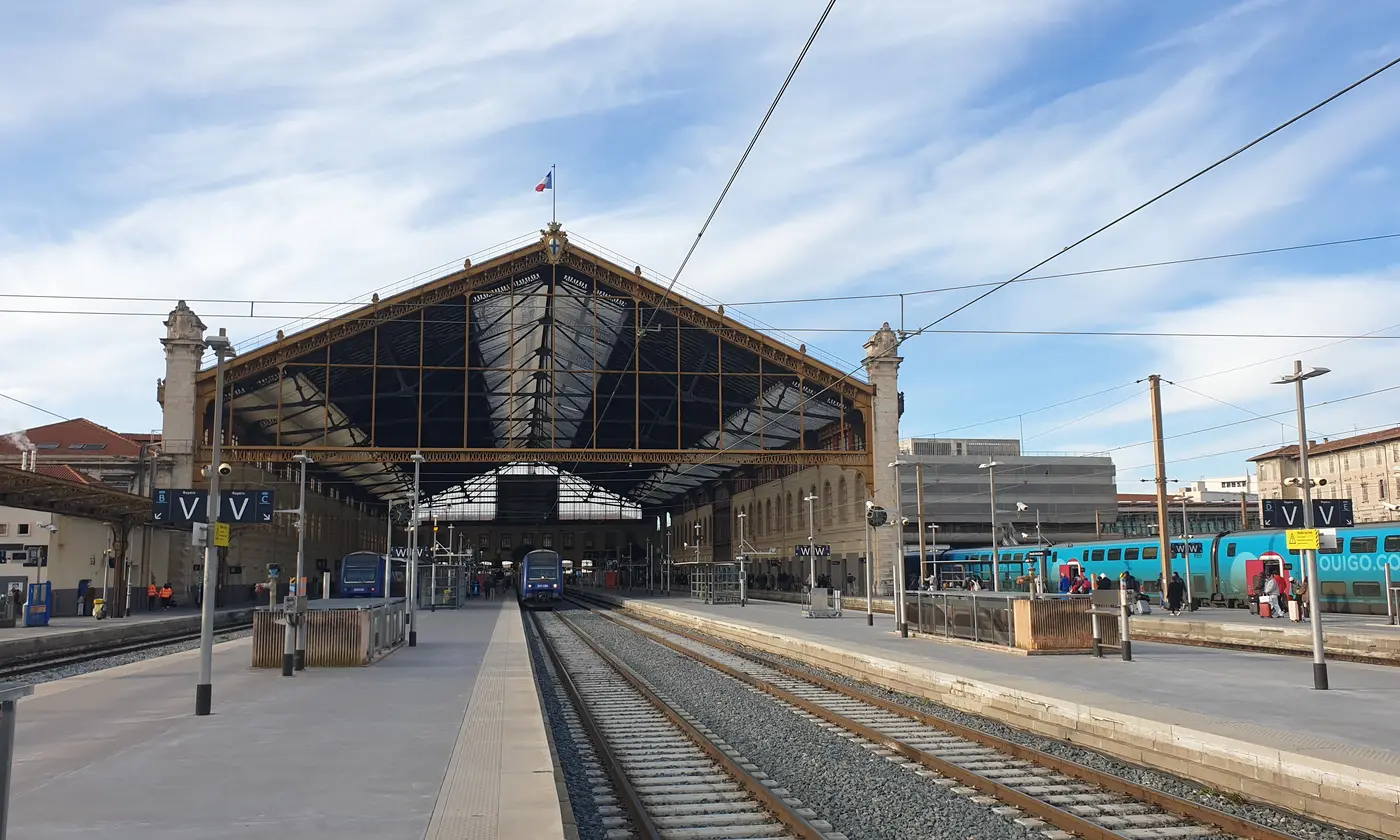Les quais de la gare Saint-Charles devant le pignon vitre de la grande halle, avec un TGV et un TER a quai.