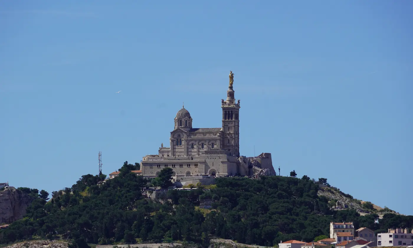 Gros plan sur la basilique Notre-Dame de la Garde et sa Bonne Mere doree, sur sa colline boisee et rocheuse, vue depuis les hauteurs de la gare Saint-Charles.