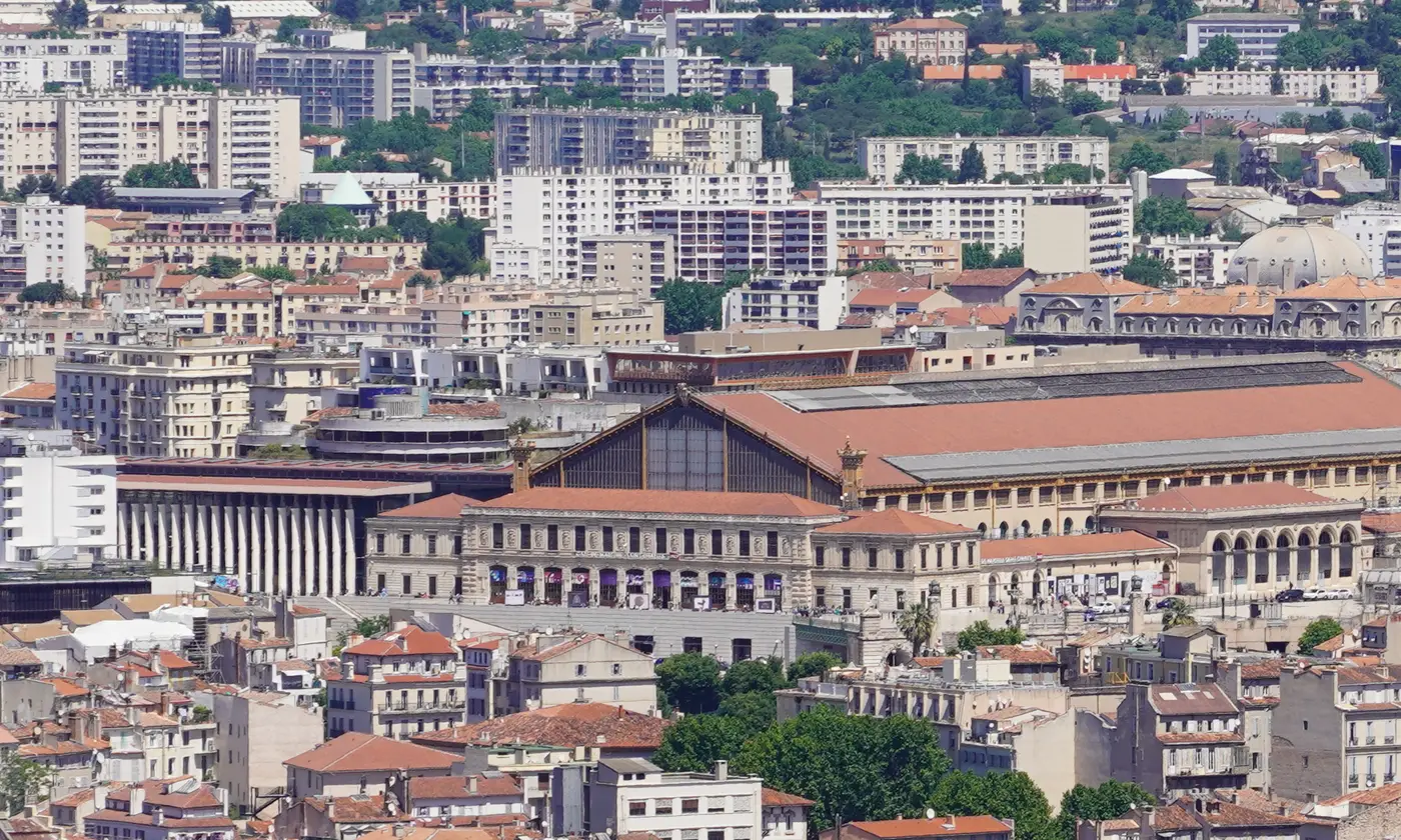 La gare Saint-Charles, sa halle et sa facade a colonnade, au milieu des toits de Marseille et des collines du nord.